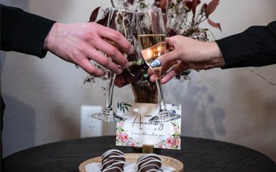 Two people clink champagne flutes over a small table