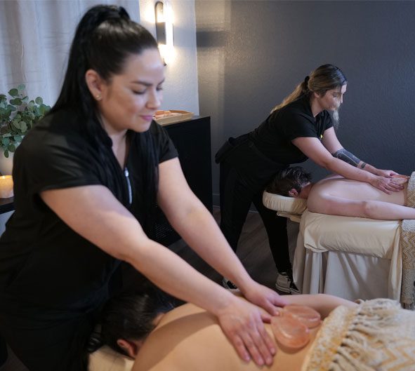 Two therapists provide a side-by-side couple's massage using heart stones.