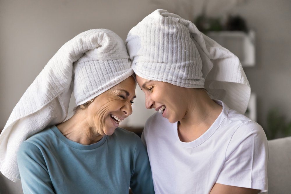 Smiling mother and daughter with spa towels on hair 2546334947 Smiling mother and daughter with spa towels on hair, forehead to forehead during a joyful mother-daughter spa day.