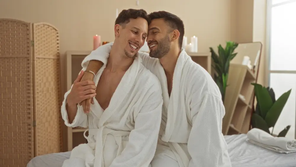 Two men in robes smiling and embracing before a relaxing partner massage session at a spa.