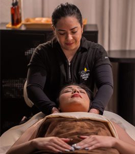 A woman relaxing while receiving a single massage hot stone treatment on her back.
